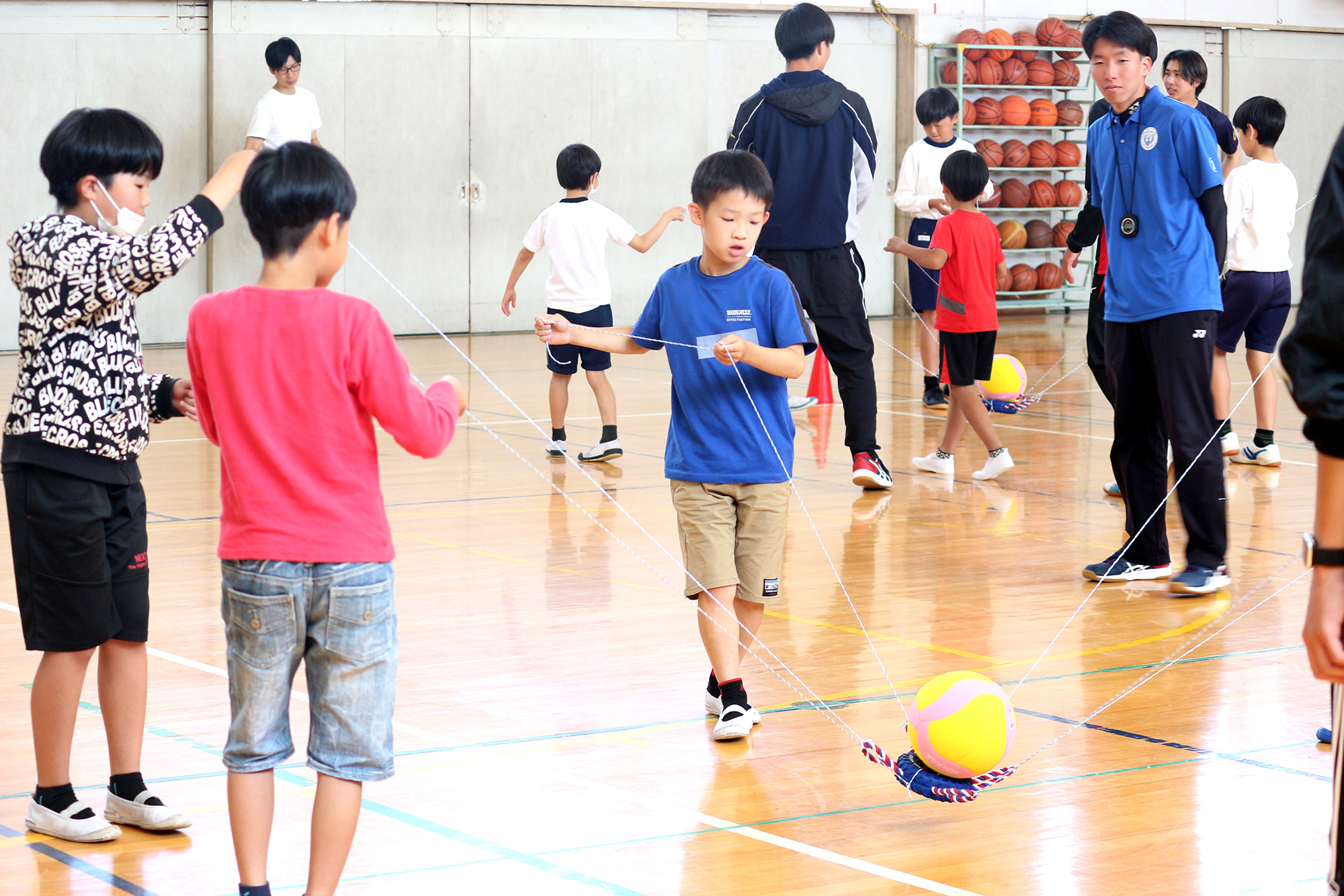 紐を持ちボールを落とさず運ぶゲームに挑戦する児童